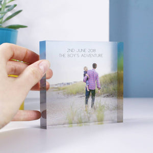 A square clear acrylic block with a photo printed onto the block, with a hand on one side of the block to give an idea of scale, this is 10cm x10cm big and is freestanding. Acrylic block with personalised text on and an image of dad holding son on the beach. 